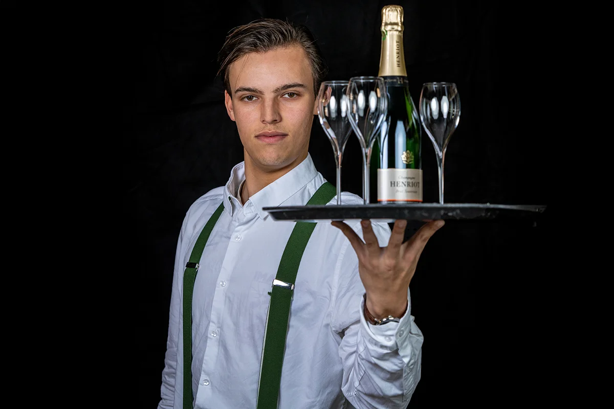 Leerling Bediening vacature bij Restaurant WOODS Leerling bediening van Restaurant WOODS presenteert champagne en glazen op een dienblad